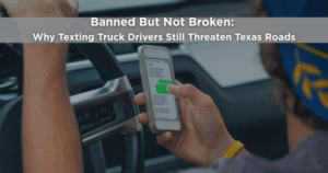 Truck driver holding a smartphone and texting while driving, illustrating the dangers of distracted commercial driving on Texas roads.